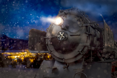 A vintage steam locomotive illuminated by its headlight, set against a snowy night backdrop with distant city lights.