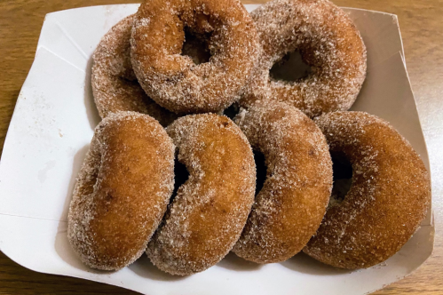 A box of freshly made, cinnamon-sugar coated donuts arranged neatly.