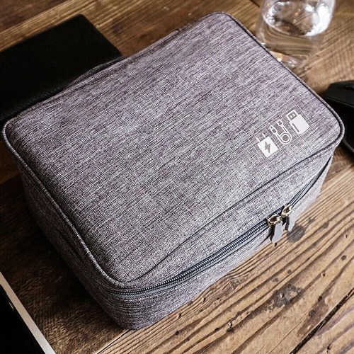 A gray zippered bag with a textured fabric, placed on a wooden table next to a glass of water and other items.