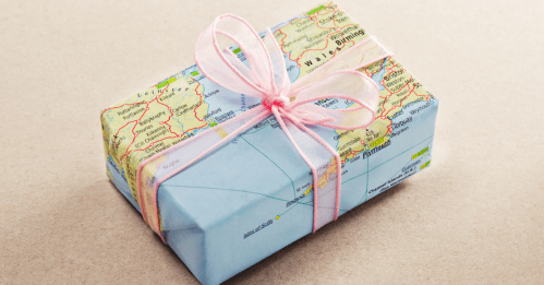 A gift wrapped in a map with a pink ribbon, resting on a brown surface.