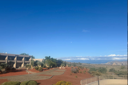 A scenic view of a landscaped area with red gravel, greenery, and a clear blue sky over distant mountains and water.