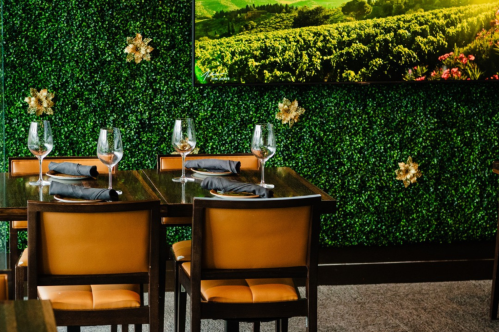 A cozy restaurant setting with wooden tables, orange chairs, and a green wall featuring a vineyard image.