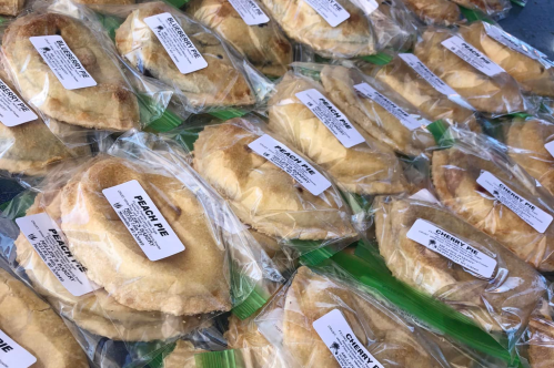 A variety of individually packaged fruit pies, labeled as peach and cherry, arranged neatly on a table.