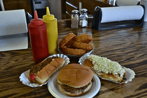A table with two hot dogs, a sandwich, onion rings, and bottles of ketchup and mustard.