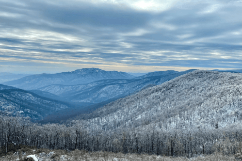 Snow-covered mountains under a cloudy sky, with layers of hills fading into the distance.