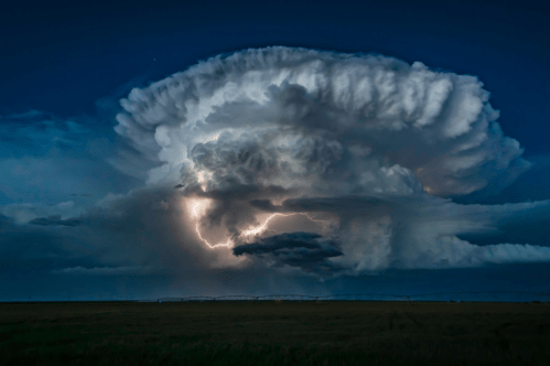 A dramatic thunderstorm cloud formation illuminated by lightning against a darkening sky.