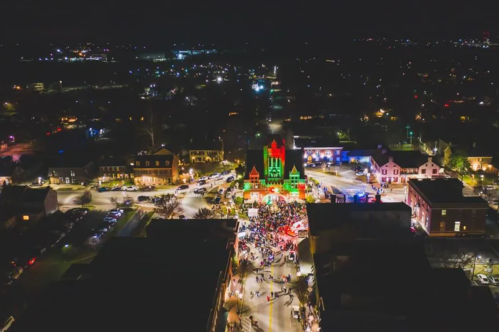 Aerial view of a festive night scene with colorful lights and a crowd gathered around a decorated building.