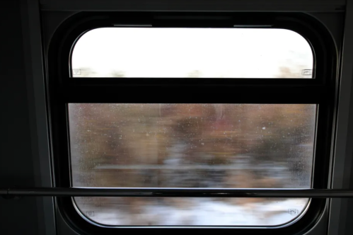 A blurred view through a train window, showcasing a landscape in motion with soft colors and reflections.
