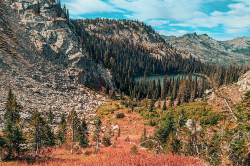A scenic view of a mountainous landscape with a lake surrounded by evergreen trees and colorful autumn foliage.
