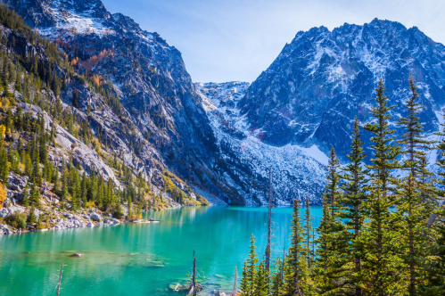 A serene turquoise lake surrounded by rocky mountains and evergreen trees under a clear blue sky.