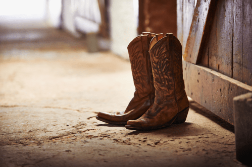 A pair of worn brown cowboy boots resting on a rustic floor near a wooden door.
