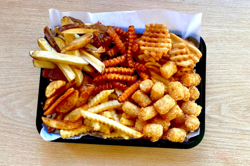 A tray filled with various types of fries: crinkle-cut, curly, waffle, and tater tots, all on a wooden surface.