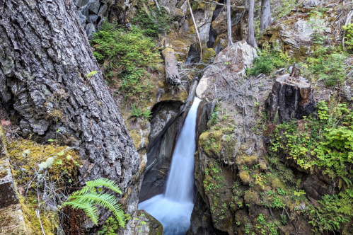A serene waterfall cascades through rocky terrain, surrounded by lush greenery and moss-covered stones.