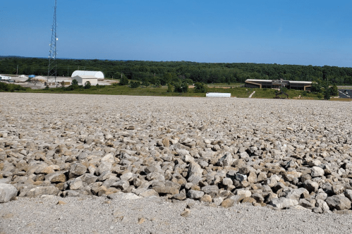A rocky landscape with a communication tower and buildings in the background, under a clear blue sky.