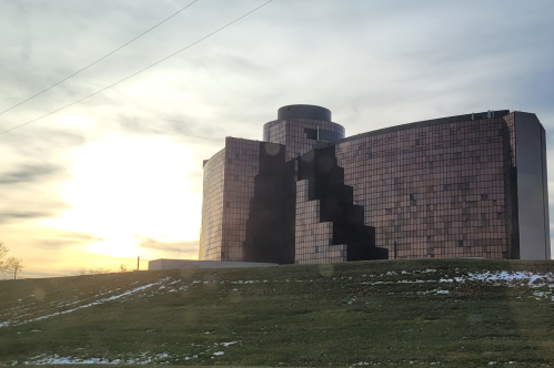 A modern building with a reflective facade, set against a cloudy sky and a grassy foreground.