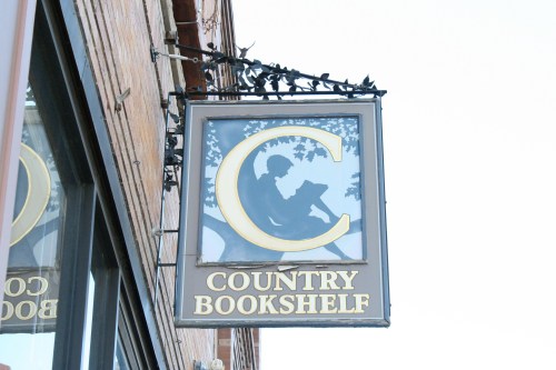 Sign for "Country Bookshelf" featuring a silhouette of a person reading under a tree.