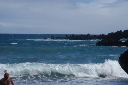 A scenic view of a rocky coastline with waves crashing against the shore under a cloudy sky.