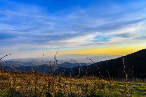 A scenic view of mountains under a colorful sky at sunset, with dry branches in the foreground.