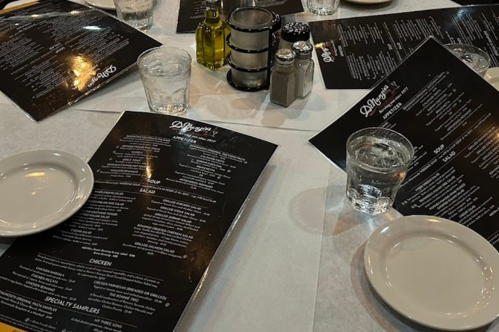 A table set with menus, plates, glasses of water, and condiments in a restaurant setting.