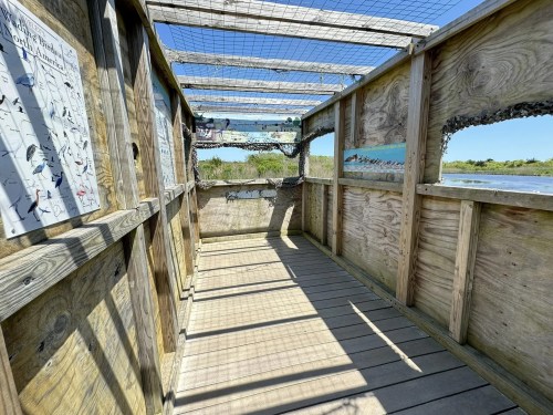A wooden observation deck with a slatted roof, overlooking a natural landscape, featuring informational signs on the walls.