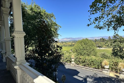 View from a porch overlooking lush vineyards and rolling hills under a clear blue sky.