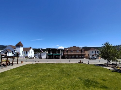 A sunny day in a small town with colorful buildings, green grass, and a clear blue sky.