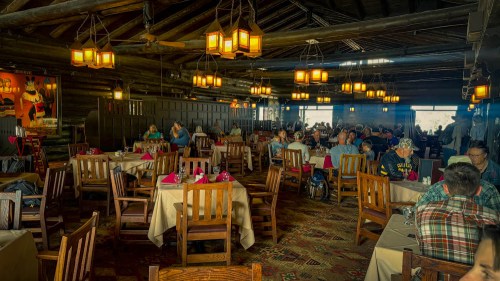 A cozy restaurant interior with wooden beams, warm lighting, and diners at tables, creating a welcoming atmosphere.