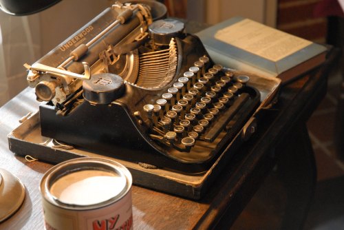 A vintage Underwood typewriter on a wooden desk, with a book and a can nearby. Soft lighting enhances the nostalgic feel.