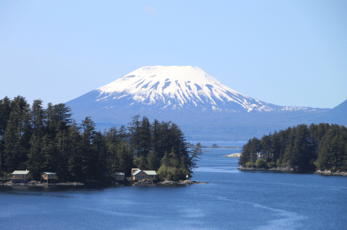 A serene landscape featuring a snow-capped mountain, lush forests, and a calm blue lake under a clear sky.
