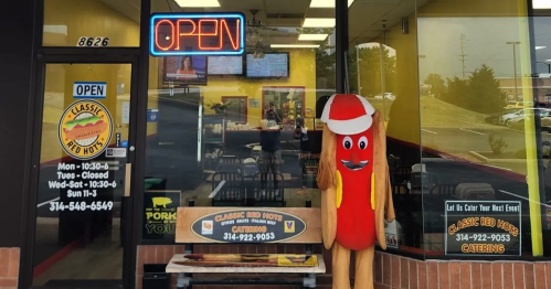 A storefront with an "OPEN" sign, featuring a large hot dog mascot outside and a bright, welcoming interior.