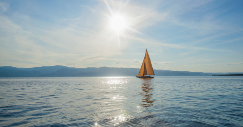 A sailboat floats in the middle of a vast, blue lake on a clear-sky day.