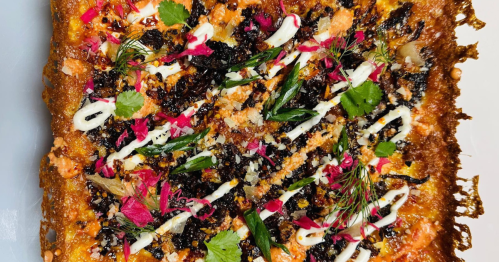 A square pizza covered with sauces, sprigs of cilantro, and pickled cabbage sits on a white cutting board.