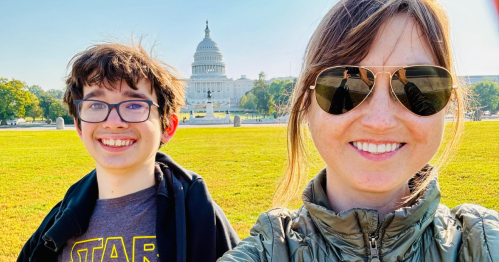 A woman and a boy smile for a selfie in front of the U.S. Capitol building on a sunny day.