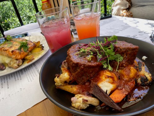 A plate of hearty meat with vegetables and sauce, accompanied by two colorful drinks on a table.