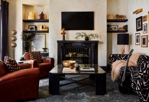 A stylish living room featuring a black fireplace, modern decor, leather chairs, and a guitar by the wall.