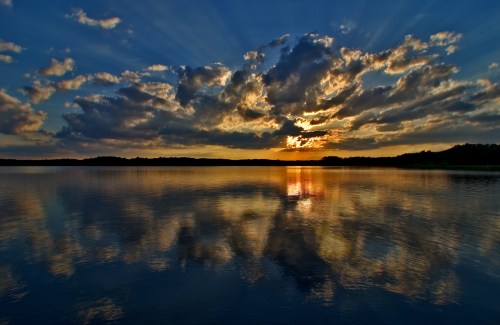 A serene lake at sunset, with vibrant clouds and golden reflections on the water's surface.