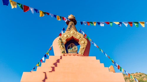 A colorful stupa adorned with prayer flags against a clear blue sky.