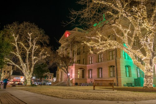 A historic building adorned with colorful holiday lights, surrounded by illuminated trees at night.