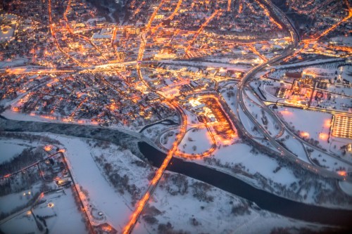 Aerial view of a snowy town at night, illuminated streets, and a winding river reflecting city lights.