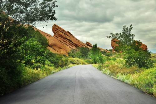 A winding road surrounded by lush greenery and striking red rock formations under a cloudy sky.