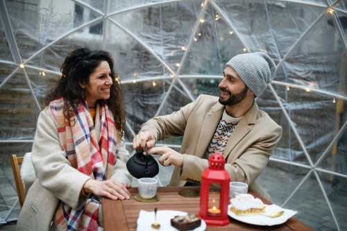 A couple enjoys tea together in a cozy igloo-like setting, smiling and sharing a warm moment.