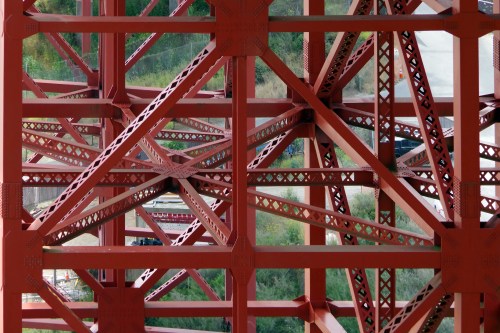 Close-up of a red metal structure showcasing intricate beams and lattice patterns against a green background.