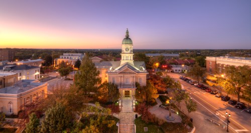 Aerial view of a historic building with a clock tower at sunset, surrounded by trees and city streets.