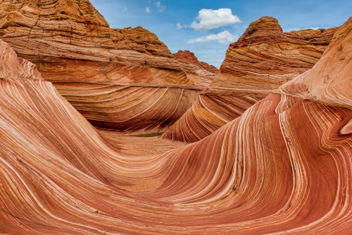 Colorful, undulating rock formations with layered textures in a desert landscape under a blue sky.