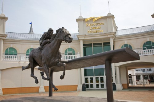 A bronze statue of a horse and jockey in front of the Kentucky Derby Museum.
