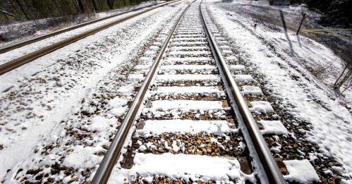 Snow-covered railway tracks stretch into the distance, flanked by gravel and a snowy landscape.