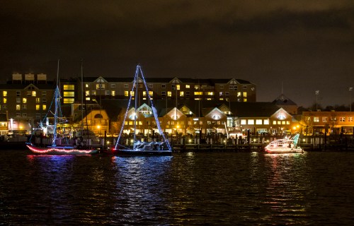 Three boats adorned with colorful lights float on a dark waterway, with a lit-up building in the background at night.