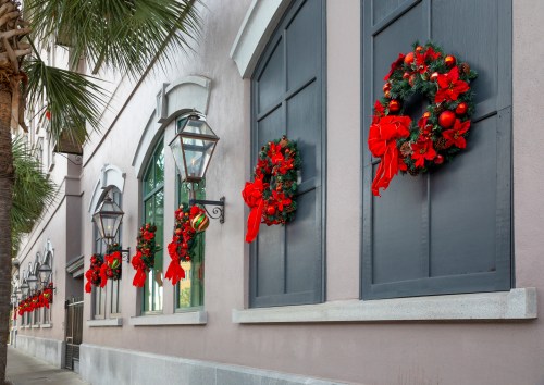 Decorated windows with festive wreaths and red bows, lined along a building's exterior, surrounded by palm trees.