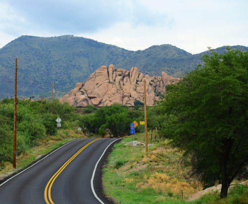 A winding road leads towards large rock formations and green hills under a cloudy sky.
