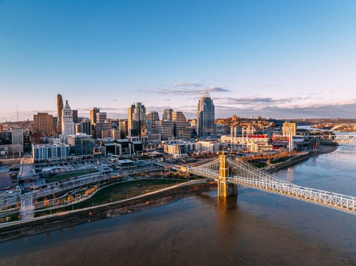 Aerial view of Cincinnati skyline with a bridge over the river, showcasing modern buildings and a clear blue sky.